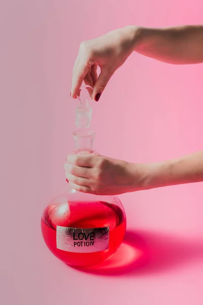 Tiro recortado de mulher frasco de abertura com poção de amor de cor vermelha na superfície rosa — Fotografia de Stock