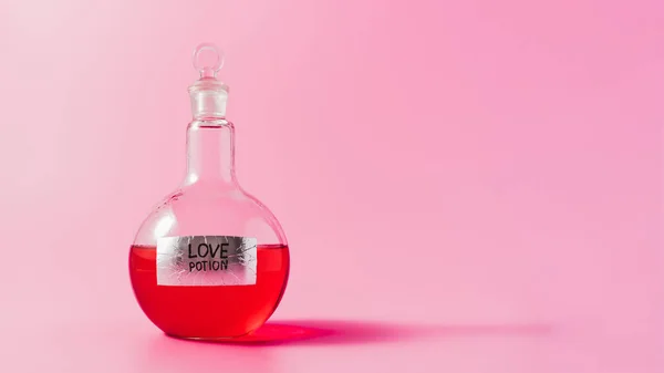 Plan rapproché de la fiole avec potion d'amour de couleur rouge sur la surface rose — Photo de stock