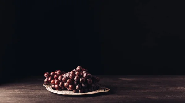 Uvas vermelhas maduras frescas na placa vintage na mesa de madeira no preto — Fotografia de Stock