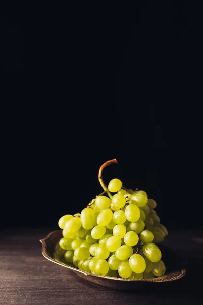 Vista close-up de uvas brancas maduras frescas na placa vintage em mesa de madeira em preto — Fotografia de Stock