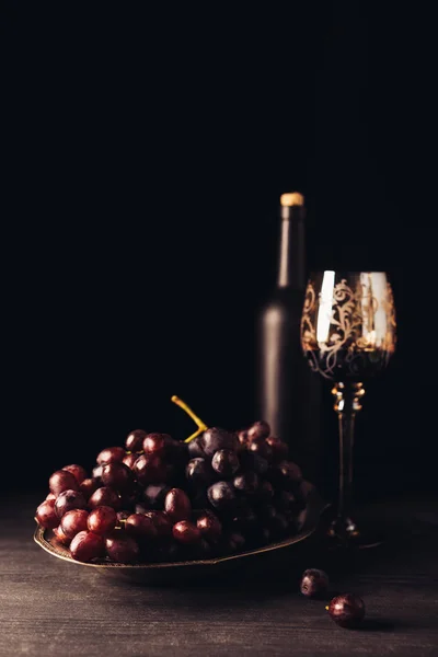 Fresh ripe grapes, glass and bottle of wine on wooden table on black — Stock Photo