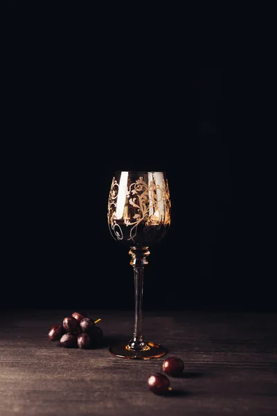 Glass of delicious red wine and fresh grapes on wooden table on black — Stock Photo