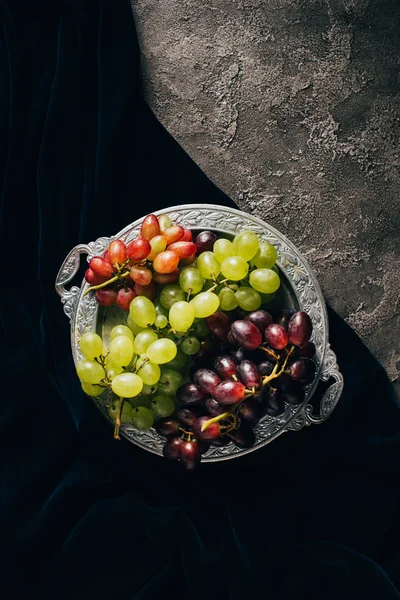 Top view of various types of grapes on vintage plate on dark fabric — Stock Photo