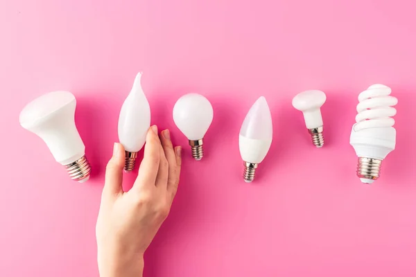 Partial top view of human hand and various types of light bulbs on pink — Stock Photo