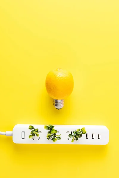 Vue de dessus de l'ampoule faite de citron et prise de sortie avec des brindilles vertes sur fond jaune — Photo de stock