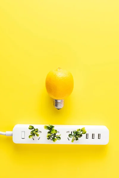 Vista dall'alto di lampadina fatta di limone e presa di corrente con ramoscelli verdi su sfondo giallo — Foto stock