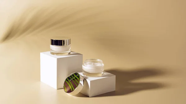 Close up vista de sombra folha de palma, facial e cremes corporais em frascos de vidro em cubos brancos no fundo bege — Fotografia de Stock
