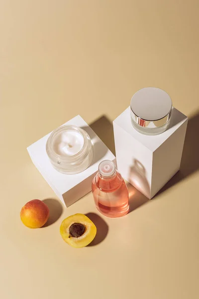 Vue rapprochée des abricots, des crèmes pour le visage et de la lotion hydratante sur fond beige — Photo de stock