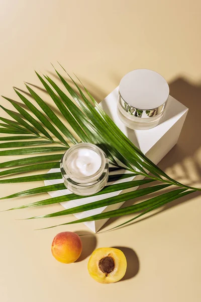 Vista de cerca de los productos para el cuidado de la piel, albaricoques y hojas de palma verde sobre fondo beige - foto de stock