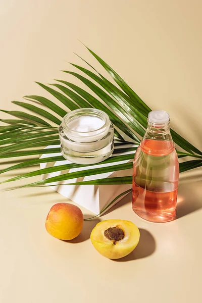 Vista da vicino di prodotti per la cura della pelle, albicocche e foglie di palma verde su sfondo beige — Foto stock