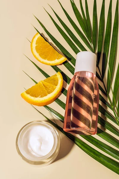 Vista dall'alto di prodotti per la cura della pelle, pezzi arancioni e foglie di palma verde su sfondo beige — Foto stock