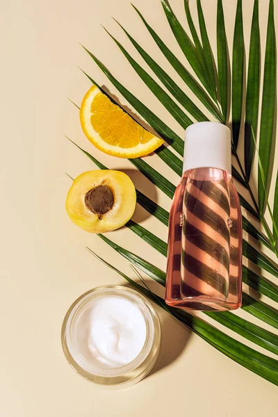 Vista superior de crema corporal y loción, frutas y hoja de palma verde sobre fondo beige - foto de stock