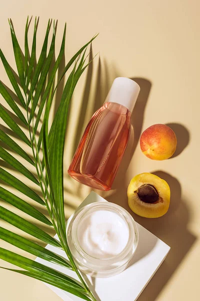 Flat lay with body cream and lotion, apricots and green palm leaf on beige background — Stock Photo