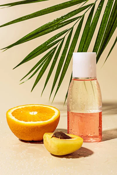 Vista de cerca del agua micelar para el cuidado de la piel en botella y mitad naranja con gotas de agua sobre fondo beige - foto de stock