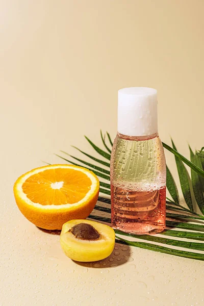 Vista de cerca del agua micelar para el cuidado de la piel en botella y mitad naranja sobre fondo beige - foto de stock
