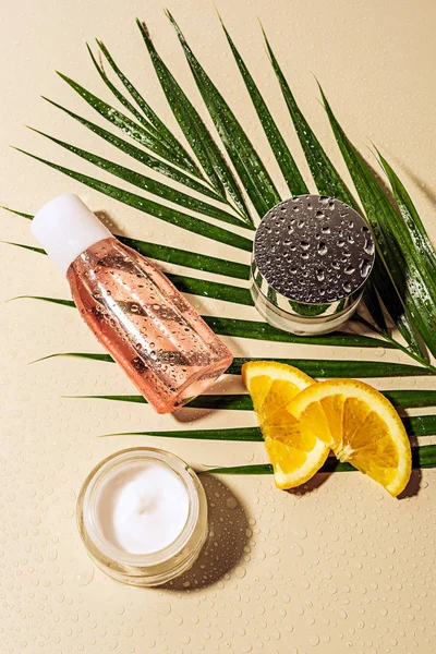 Flat lay with skin care products, green palm leaf and orange slices with water drops on beige backdrop — Stock Photo