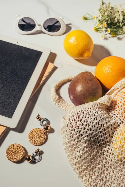 Vista superior de tablet digital, brincos, óculos de sol, flores e saco de cordas com frutas tropicais maduras frescas em branco — Fotografia de Stock