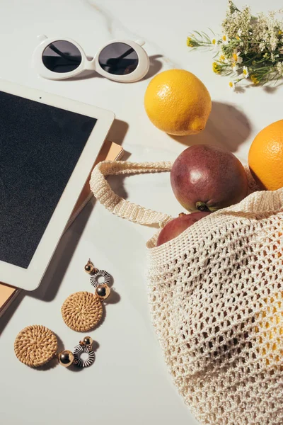Vista ravvicinata di tablet digitale, occhiali da sole, orecchini, fiori e sacchetto di spago con frutta tropicale fresca — Foto stock