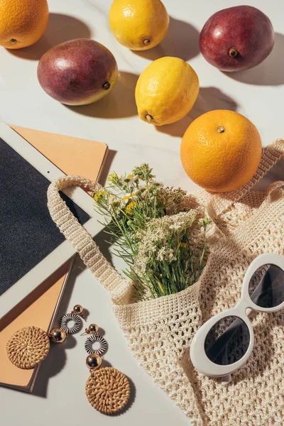 Vista superior de la tableta digital, pendientes, gafas de sol, flores y bolsa de hilo con frutas frescas maduras - foto de stock