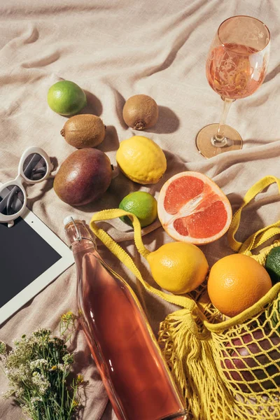 Вид сверху на стекло и бутылку с летним напитком, цифровой планшет, солнцезащитные очки и струнный мешок со свежими фруктами — стоковое фото