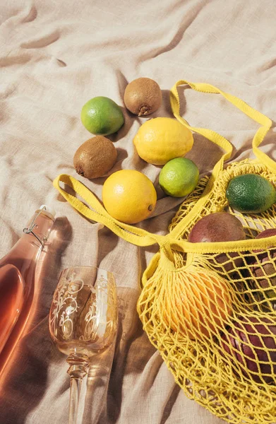 Vista superior de vidrio, botella con bebida de verano y bolsa de hilo amarillo con frutas tropicales frescas maduras — Stock Photo