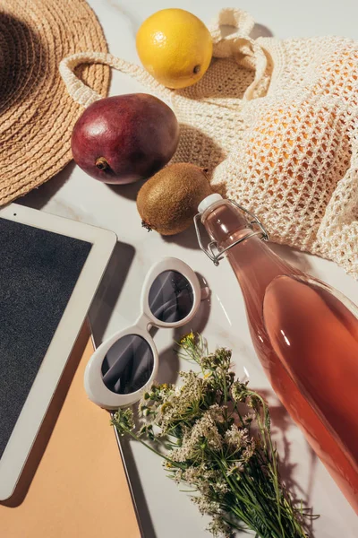 Vista superior de sombrero de paja, tableta digital, botella de vidrio con bebida de verano y bolsa de cuerda con frutas frescas — Stock Photo