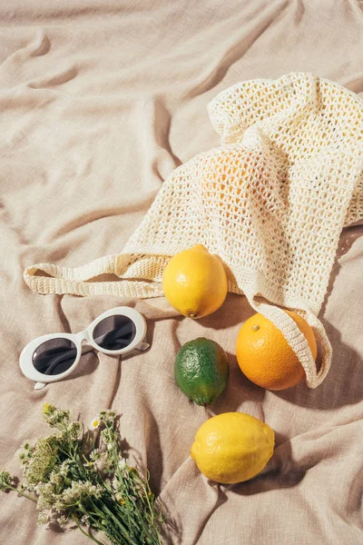 Vista en ángulo alto de gafas de sol, flores y bolsa de hilo con frutas tropicales - foto de stock