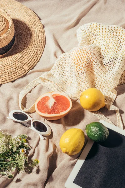 Vista superior de sombrero de mimbre, gafas de sol, flores, tableta digital y bolsa de cuerda con frutas frescas - foto de stock