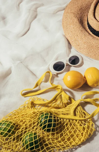 Vista de ángulo alto de gafas de sol, sombrero de mimbre y bolsa de hilo con frutas tropicales maduras frescas - foto de stock