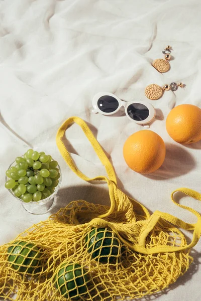 Blick auf Sonnenbrille, Ohrringe und gelben Schnurbeutel mit frischen Früchten — Stockfoto