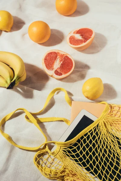 Tableta digital en bolsa de hilo amarillo y frutas tropicales frescas maduras - foto de stock