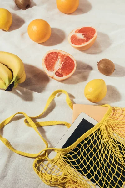 Vue du dessus du sac à ficelle jaune avec tablette numérique et fruits tropicaux frais mûrs — Photo de stock