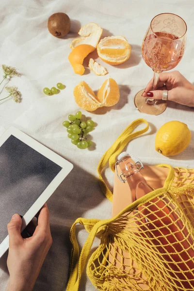 Cropped shot of human hands with glass, digital tablet and string bag with ripe fruits — Stock Photo