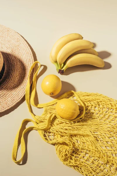 Top view of straw hat and yellow string bag with lemons and bananas — Stock Photo