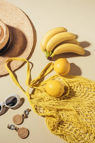 Vue du haut du chapeau en osier, lunettes de soleil, boucles d'oreilles et sac à ficelle jaune avec bananes et citrons — Photo de stock