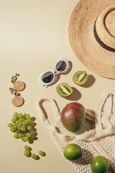 Vista dall'alto di cappello di vimini, occhiali da sole, orecchini e sacchetto di corda con frutta fresca — Foto stock