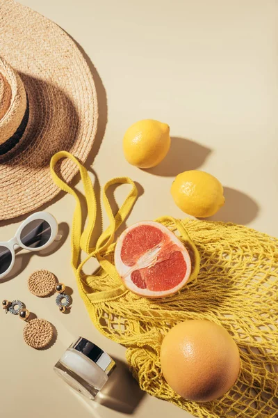 Top view of wicker hat, sunglasses, earrings, cream and string bag with fruits — Stock Photo