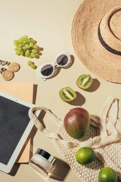 Vista superior de óculos de sol, chapéu, tablet digital e saco de cordas com creme e frutas maduras frescas — Fotografia de Stock