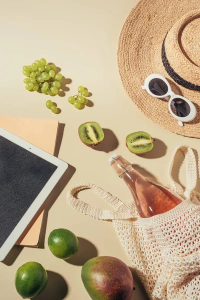 Vista superior de gafas de sol, sombrero, tableta digital y bolsa de hilo con bebida y frutas - foto de stock