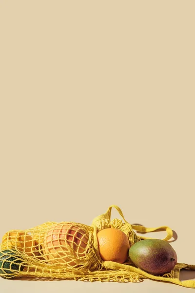 Close-up view of yellow string bag with ripe tropical fruits on brown background — Stock Photo