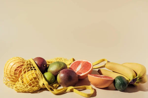 Vue rapprochée des fruits tropicaux frais mûrs et sac à ficelle sur brun — Photo de stock