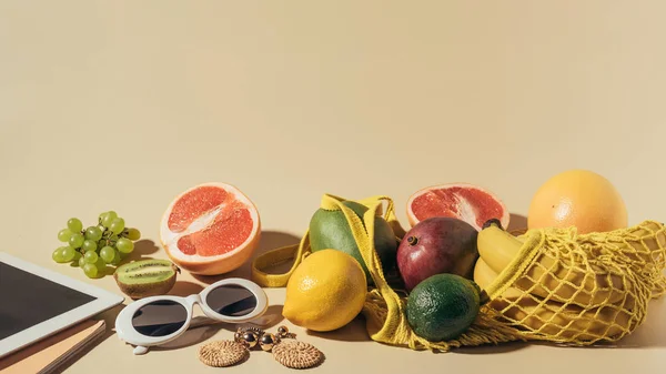 Vista close-up de óculos de sol, brincos, tablet digital e frutas maduras em saco de cordas em marrom — Fotografia de Stock