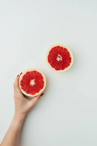 Visión parcial de la mujer sosteniendo mitades de pomelo, en gris - foto de stock