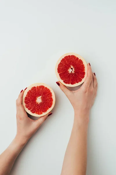 Vista recortada de la mujer sosteniendo mitades de pomelo, en gris — Stock Photo