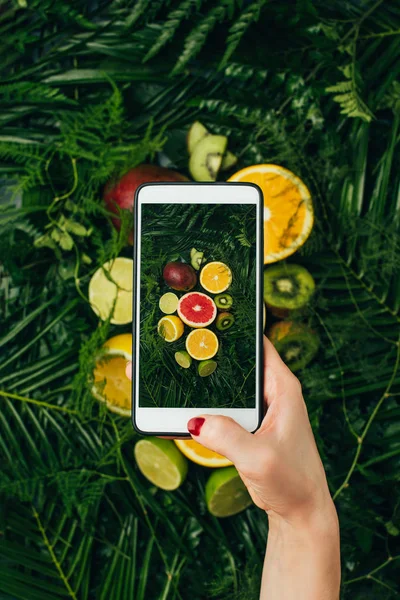 Vista recortada del bloguero de alimentos tomando fotos de frutas frescas en el teléfono inteligente - foto de stock