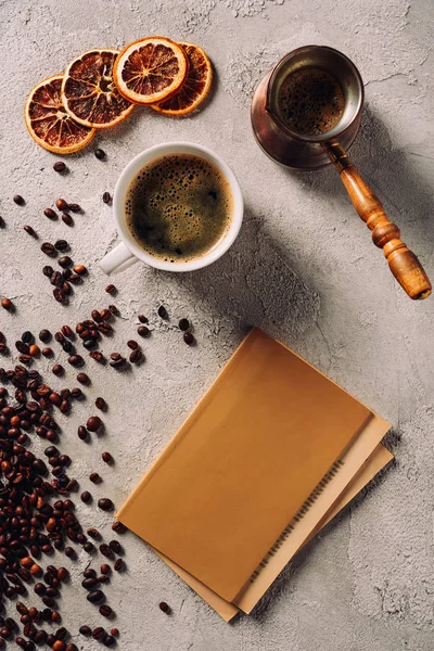 Vue de dessus de tasse et cezve de café avec livre sur la surface du béton — Photo de stock