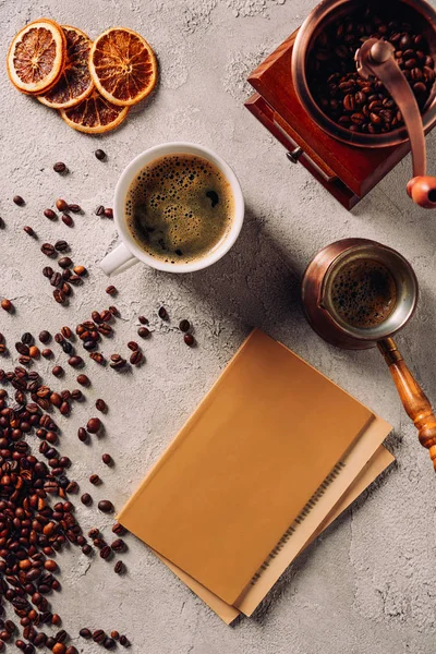 Vue de dessus de tasse et cezve de café avec livre et moulin à café sur la surface du béton — Photo de stock