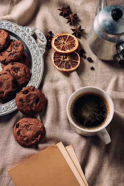 Вид сверху на чашку кофе с книгой и шоколадным печеньем на бежевой ткани — стоковое фото