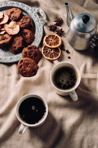 Vue du dessus des tasses de café avec biscuits aux pépites de chocolat et pot en métal vintage sur tissu beige — Photo de stock