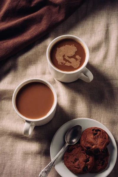 Vista superior de xícaras de café com biscoitos de chocolate em pano bege — Fotografia de Stock